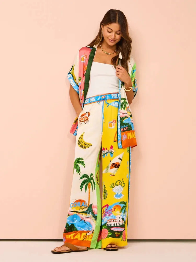 Frau in bunter Sommerkleidung mit tropischen Motiven, bestehend aus Hemd und Hose. Perfekt für Strandmode und lässige Sommeroutfits.