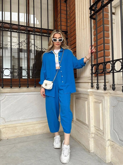 Frau in blauem Oversize-Anzug, weißem Crop-Top und Sneakers posiert vor Backsteinwand. Modetrend, Streetstyle, lässig, urban, stilvoll.