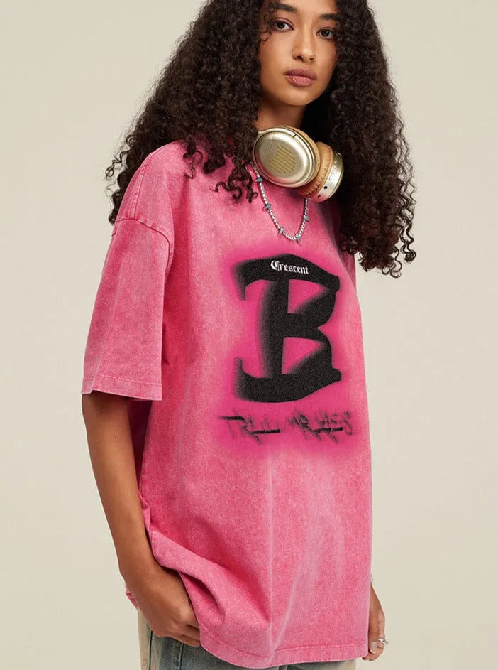 Frau mit lockigem Haar trägt ein pinkes Oversize-T-Shirt mit schwarzem Graffiti-Design und Kopfhörern. Streetwear, urbaner Stil, modisch.