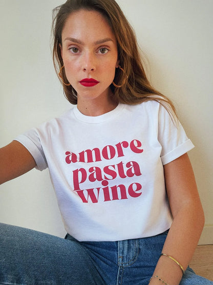 Frau trägt weißes T-Shirt mit rotem Aufdruck "amore pasta wine", kombiniert mit blauen Jeans. Modetrend, lässiger Stil, Statement-Shirt.