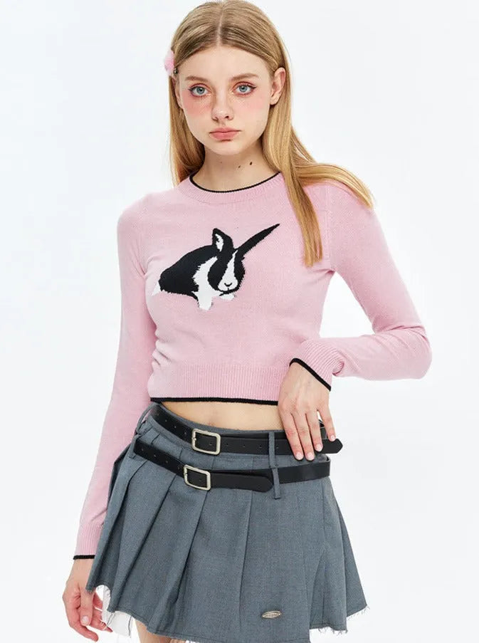 Junge Frau in rosa Pullover mit Kaninchenmotiv, grauem Faltenrock und Gürtel. Modetrend, Streetwear, stilvolle Damenbekleidung.