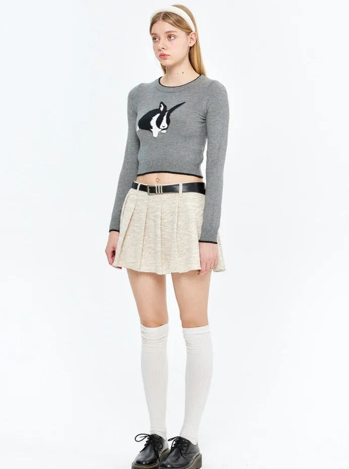 Graues Langarmshirt mit Hasenmotiv, kombiniert mit beigem Faltenrock und Kniestrümpfen. Modetrend, Damenbekleidung, Streetwear.