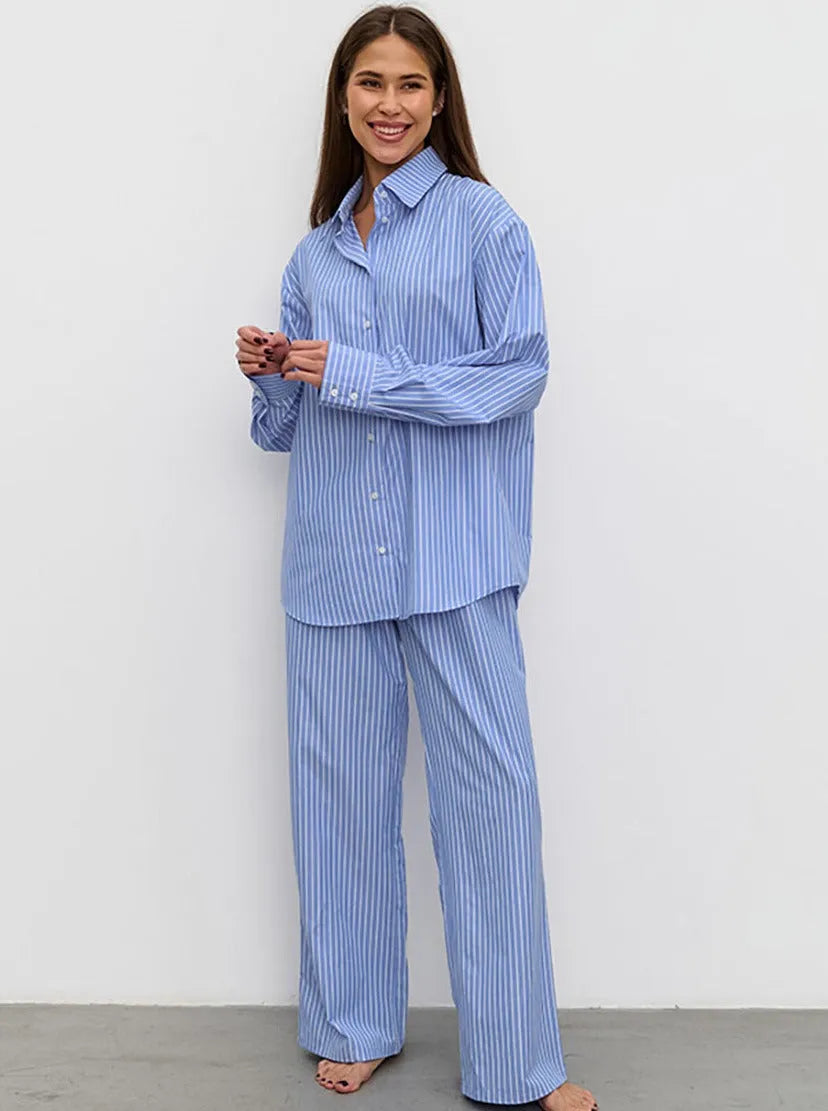 Frau in blau-weiß gestreiftem Pyjama-Set, lächelnd, vor weißem Hintergrund. Bequemes Nachtwäsche-Outfit, ideal für entspannte Abende zu Hause.