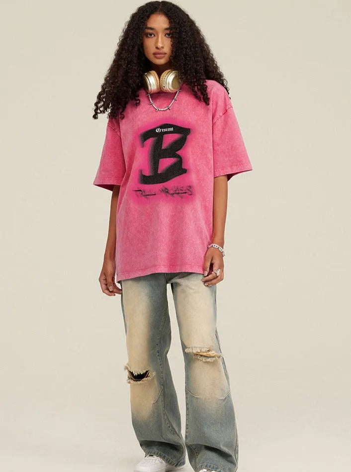 Frau in rosa Oversize-T-Shirt mit schwarzem "B"-Logo, zerrissene Jeans, Kopfhörer um den Hals. Streetwear, lässiger Stil, Mode 2023.