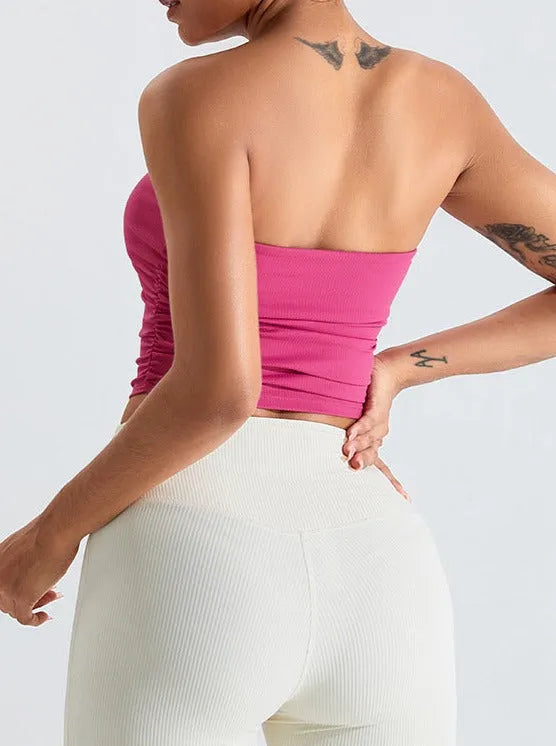 Frau in rosa trägerlosem Top und weißen Leggings, zeigt Rückenansicht. Modetrend, sportlich, elegant, Sommeroutfit, Damenbekleidung.