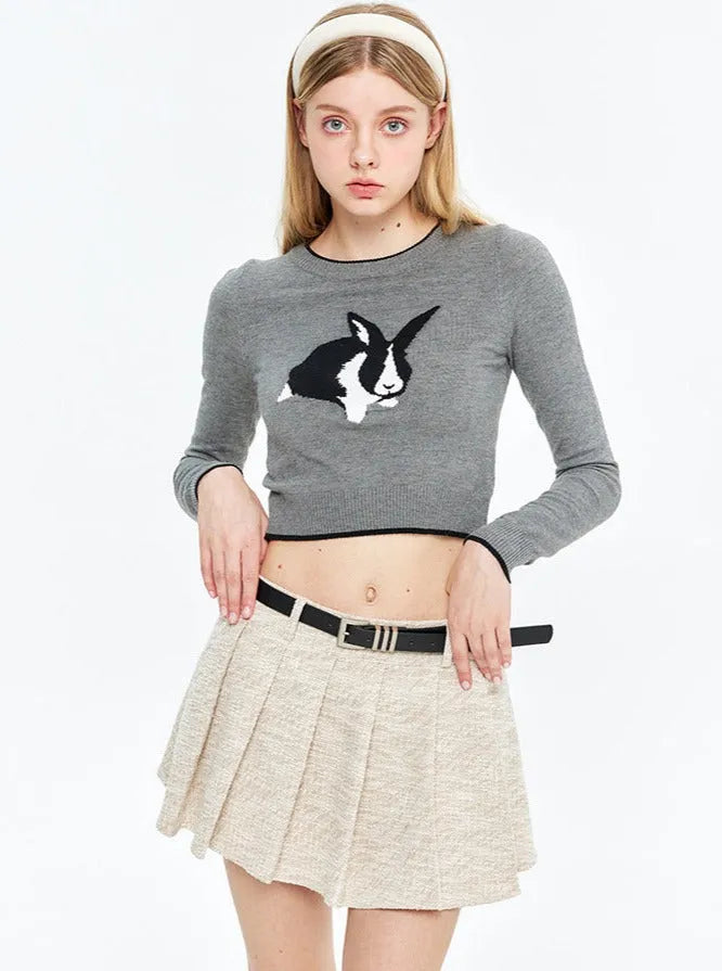 Grauer Pullover mit Hasenmotiv, kombiniert mit beigem Faltenrock. Modetrend, Damenbekleidung, stilvoller Look, Herbstmode.