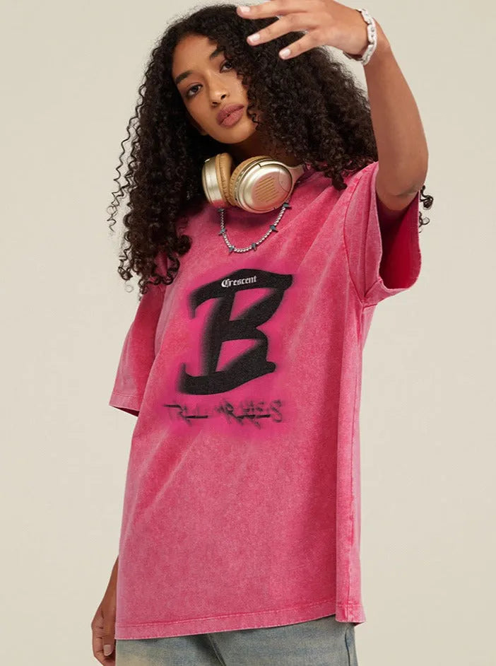 Junge Frau in rotem Oversize-T-Shirt mit schwarzem "B"-Logo, goldenen Kopfhörern um den Hals. Trendige Streetwear, urbaner Stil, lässige Mode.