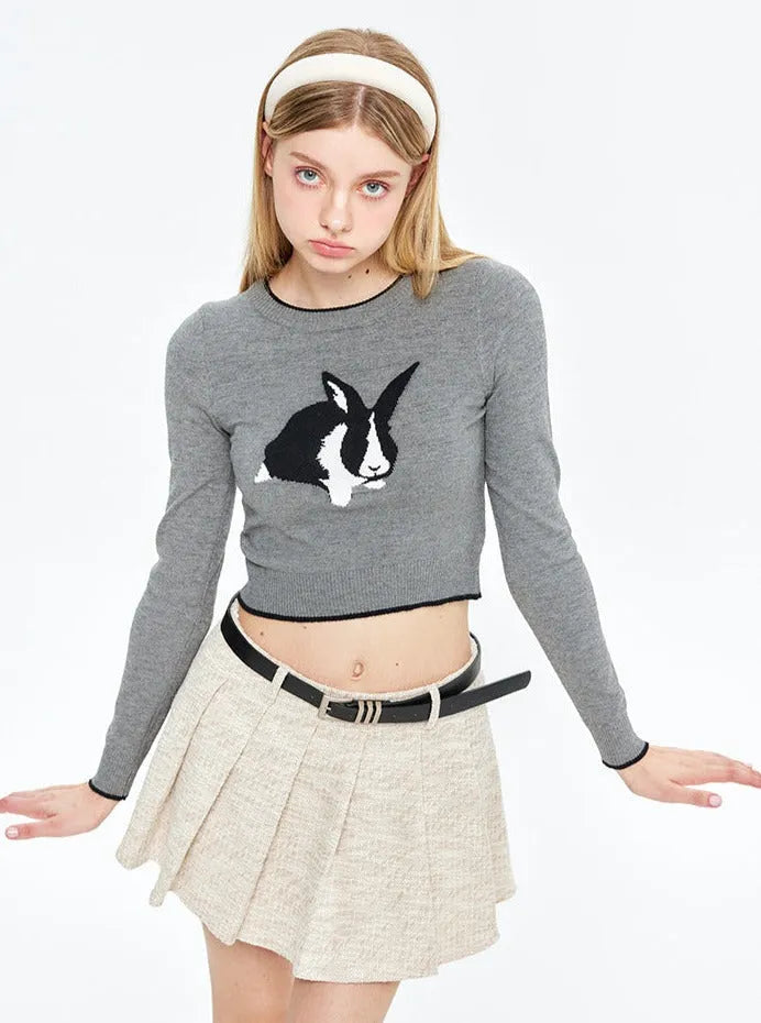 Grauer Pullover mit Hasenmotiv, kombiniert mit beigem Faltenrock und schwarzem Gürtel. Modetrend, Damenmode, Herbstkollektion.