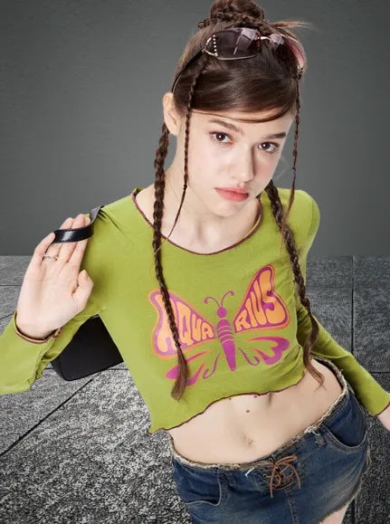 Junge Frau in grünem Crop-Top mit Schmetterlingsmotiv, Jeansrock und Sonnenbrille. Trendige Mode, Streetwear, lässiger Stil, jugendlicher Look.