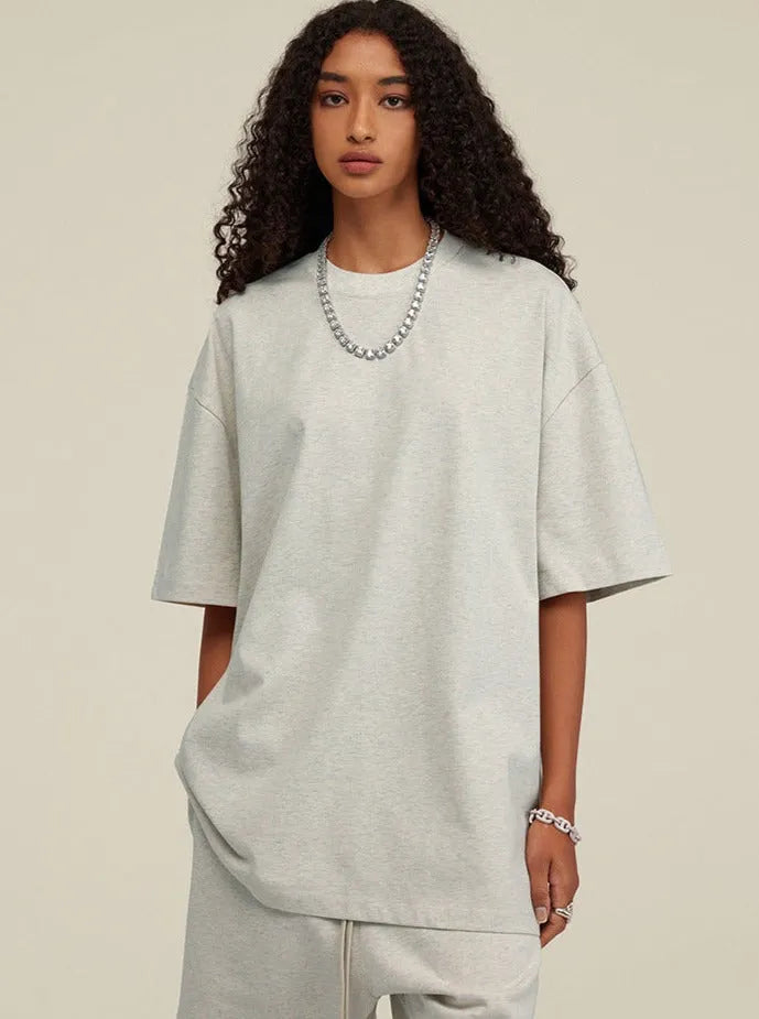 Frau in grauem Oversize-T-Shirt und Jogginghose, modisch mit lockigem Haar und Kette. Trendige Streetwear, lässiger Look, urbaner Stil.