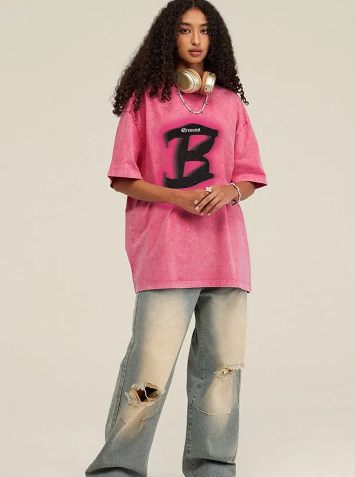 Frau in rosa Oversize-T-Shirt mit großem "B"-Logo, zerrissene Jeans, Kopfhörer um den Hals. Modetrend, Streetwear, lässiger Stil.