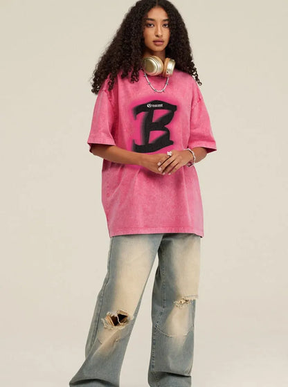 Frau in rosa Oversize-T-Shirt mit großem "B"-Logo, zerrissene Jeans, Kopfhörer um den Hals. Modetrend, Streetwear, lässiger Stil.