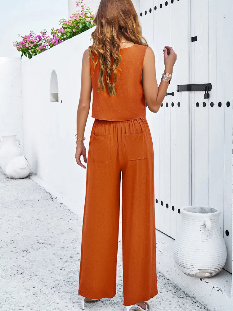 Frau in orangefarbenem Jumpsuit vor weißer Wand, Sommermode, lässiger Stil, ärmelloses Top, weite Hose, modische Damenbekleidung.