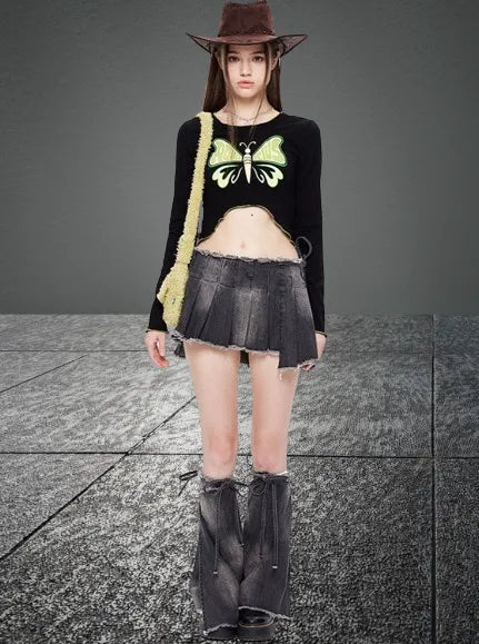 Junge Frau in modischer Kleidung: schwarzes Crop-Top mit Schmetterlingsmotiv, grauer Minirock, Cowboystiefel, brauner Hut. Trendige Streetwear.