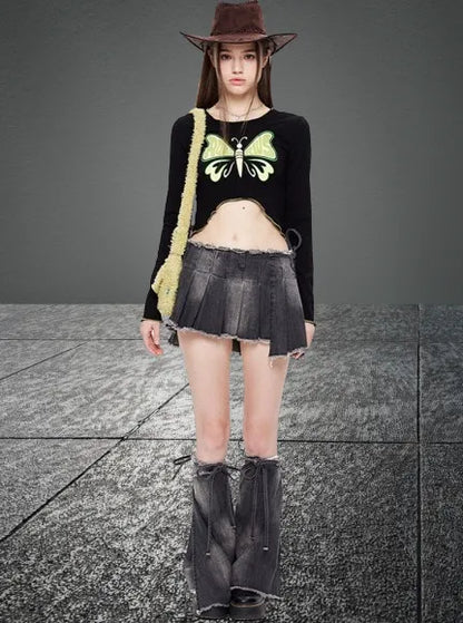 Junge Frau in modischer Kleidung: schwarzes Crop-Top mit Schmetterlingsmotiv, grauer Minirock, Cowboystiefel, brauner Hut. Trendige Streetwear.