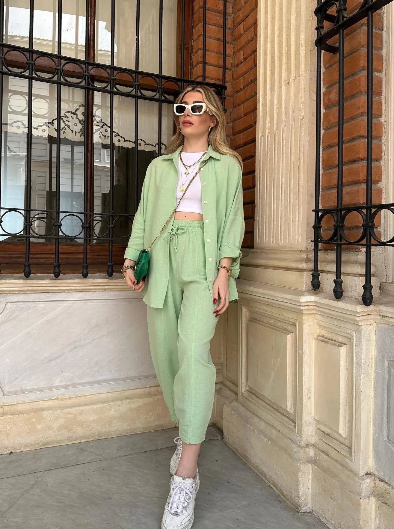 Frau in mintgrünem Anzug, weißem Crop-Top und Sneakers, posiert vor Backsteinwand. Modetrend, Streetstyle, Sommermode, lässig-elegant.