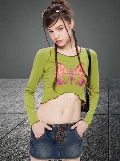 Junge Frau in grünem Langarmshirt mit Schmetterlingsmotiv und Jeansrock. Modetrend, Streetwear, lässiger Look, jugendlicher Stil.