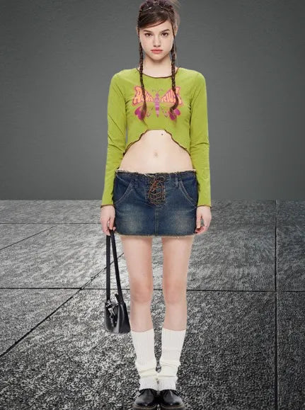 Junge Frau in grünem Crop-Top und Jeansrock, trägt weiße Socken und schwarze Schuhe, hält eine schwarze Tasche. Modetrend, Streetstyle, urban.