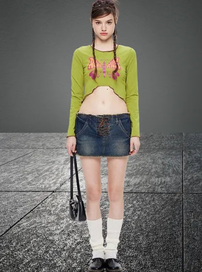 Junge Frau in grünem Crop-Top und Jeansrock, trägt weiße Socken und schwarze Schuhe, hält eine schwarze Tasche. Modetrend, Streetstyle, urban.