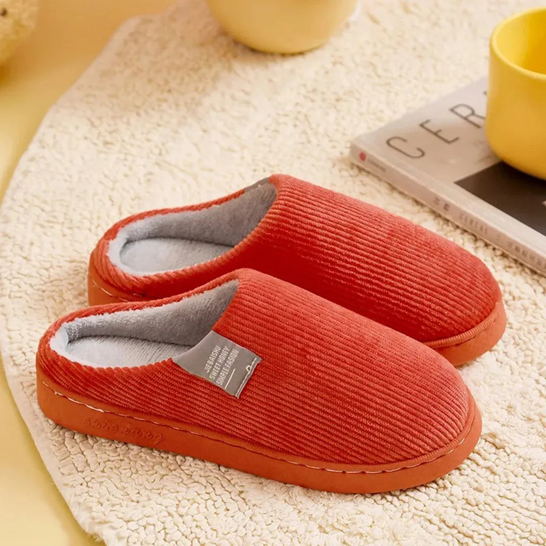 Warme, orange Hausschuhe aus weichem Cordstoff auf Teppich, ideal für gemütliche Winterabende. Perfekte Kombination aus Komfort und Stil.