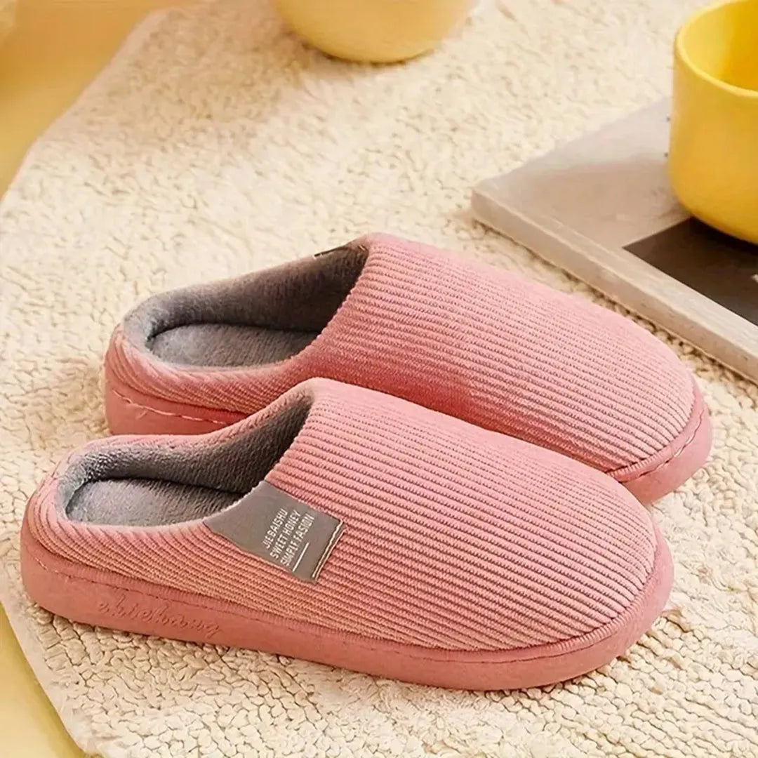 Weiche rosa Hausschuhe aus Cord auf Teppich, ideal für gemütliche Winterabende. Bequeme, warme Pantoffeln für Damen und Herren.
