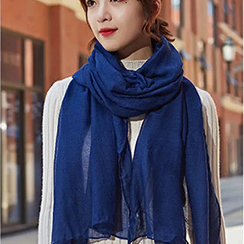 Frau mit blauem Schal und weißem Pullover auf städtischer Straße. Modetrend, Herbstmode, stilvoller Schal, Damenbekleidung, urbaner Look.