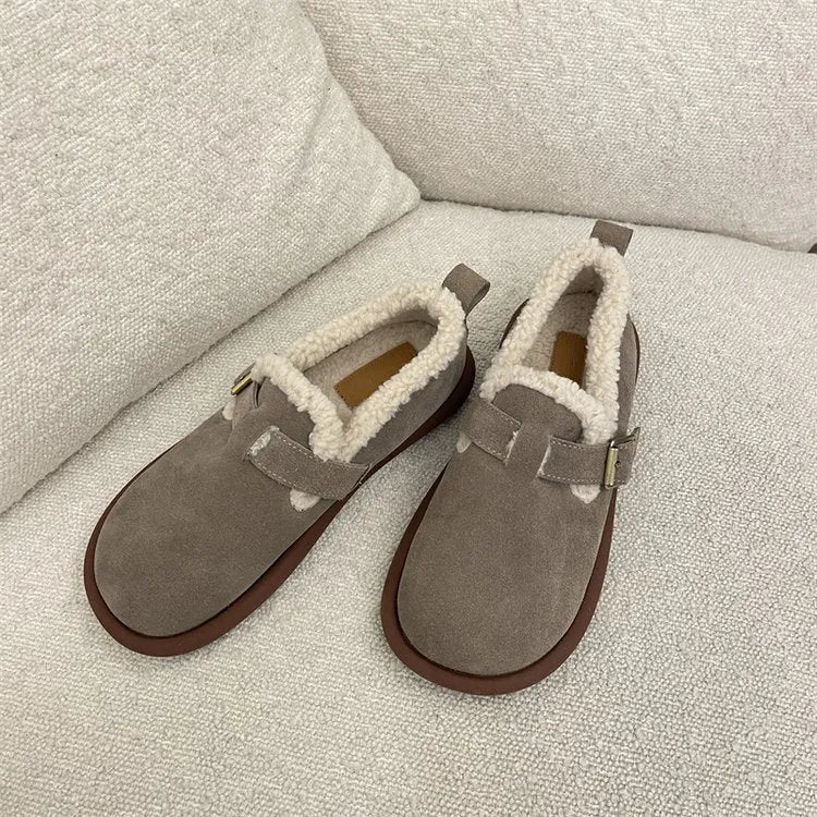 Beige Hausschuhe aus Wildleder mit weichem Futter auf beigem Sofa. Gemütliche, warme Pantoffeln für Damen. Ideal für den Winter.
