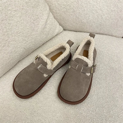 Beige Hausschuhe aus Wildleder mit weichem Futter auf beigem Sofa. Gemütliche, warme Pantoffeln für Damen. Ideal für den Winter.