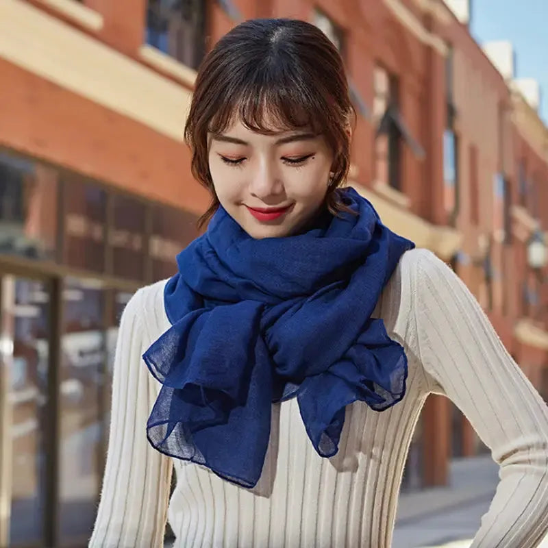Frau mit blauem Schal und weißem Pullover vor städtischer Kulisse. Modetrend, Herbstmode, stilvolle Accessoires, Damenbekleidung.