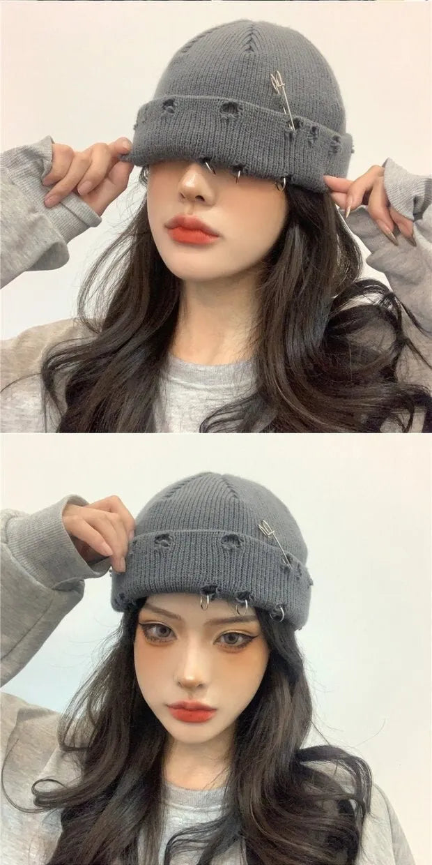 Graue Strickmütze mit Sicherheitsnadeln, getragen von einer Frau. Modisches Accessoire, ideal für Herbst- und Wintertrends. Streetwear-Style.