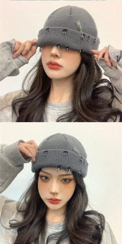 Graue Strickmütze mit Sicherheitsnadeln, getragen von einer Frau. Modisches Accessoire, ideal für Herbst- und Wintertrends. Streetwear-Style.
