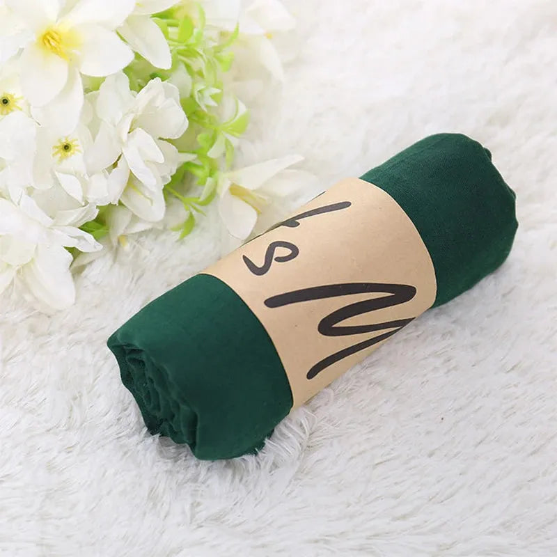 Grünes T-Shirt, gerollt und mit braunem Papierband umwickelt, auf weißem Fellteppich neben weißen Blumen. Ideal für nachhaltige Mode.