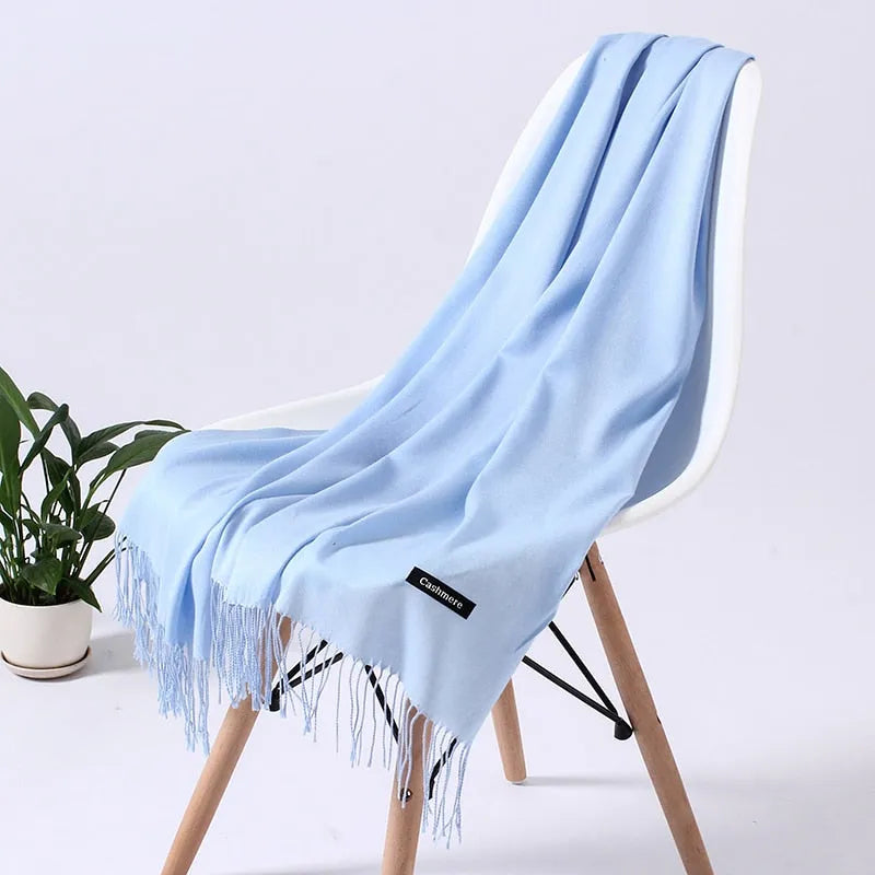 Weicher blauer Kaschmirschal auf weißem Stuhl, ideal für stilvolle Wintermode. Luxuriöses Accessoire, perfekt für kalte Tage.