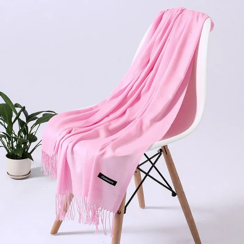 Weicher, rosa Kaschmirschal auf weißem Stuhl, ideal für stilvolle Wintermode. Luxuriöses Accessoire, perfekt für Damenbekleidung.