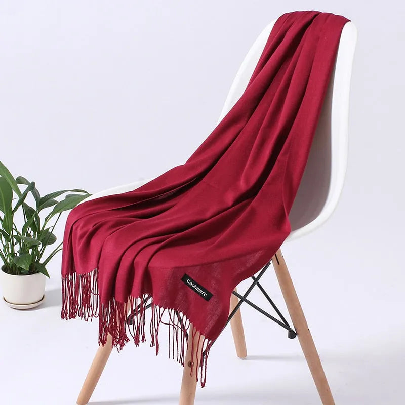 Roter Kaschmirschal auf weißem Stuhl, weiche Fransen, luxuriöses Accessoire, ideal für Herbst und Winter, stilvoll und elegant.