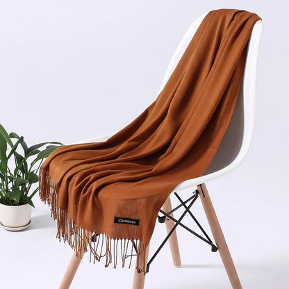 Kuscheliger Kaschmirschal in warmem Braun, drapiert über einem modernen weißen Stuhl. Perfekt für stilvolle Herbst- und Wintermode.