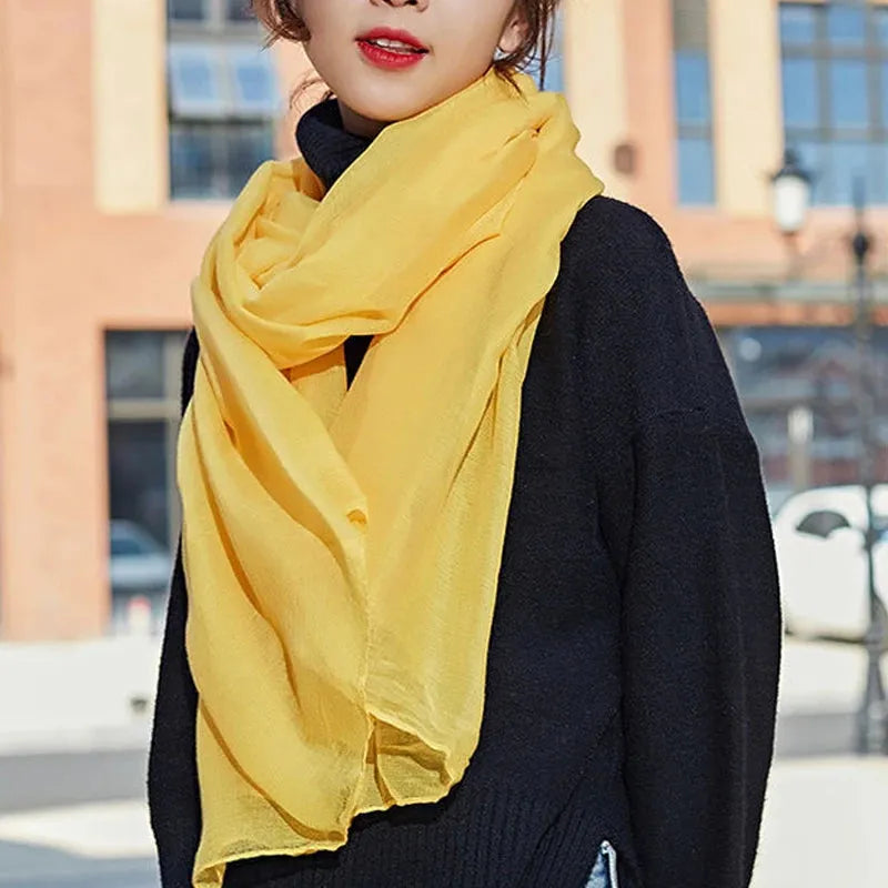 Frau mit gelbem Schal und schwarzem Pullover vor städtischer Kulisse. Modetrend, Herbstmode, Damenaccessoires, stilvoller Look.