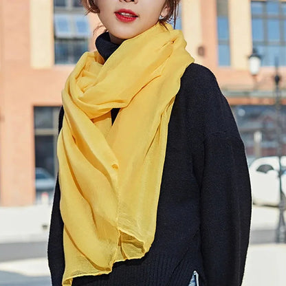 Frau mit gelbem Schal und schwarzem Pullover vor städtischer Kulisse. Modetrend, Herbstmode, Damenaccessoires, stilvoller Look.