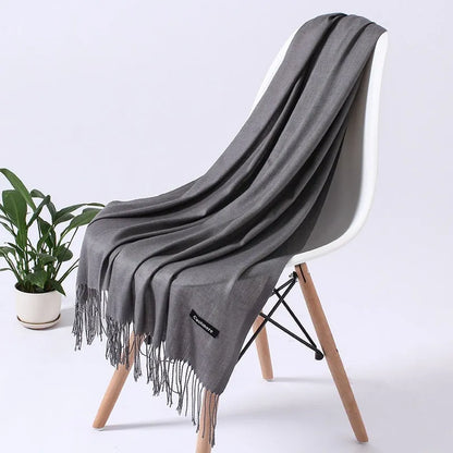 Grauer Schal aus Kaschmir auf weißem Stuhl, elegantes Design, weiche Textur, ideal für Herbst und Winter, modisches Accessoire.