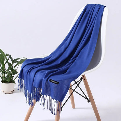 Kuscheliger blauer Kaschmirschal auf weißem Stuhl, ideal für stilvolle Wintermode. Luxuriös, weich, hochwertig, perfektes Accessoire.