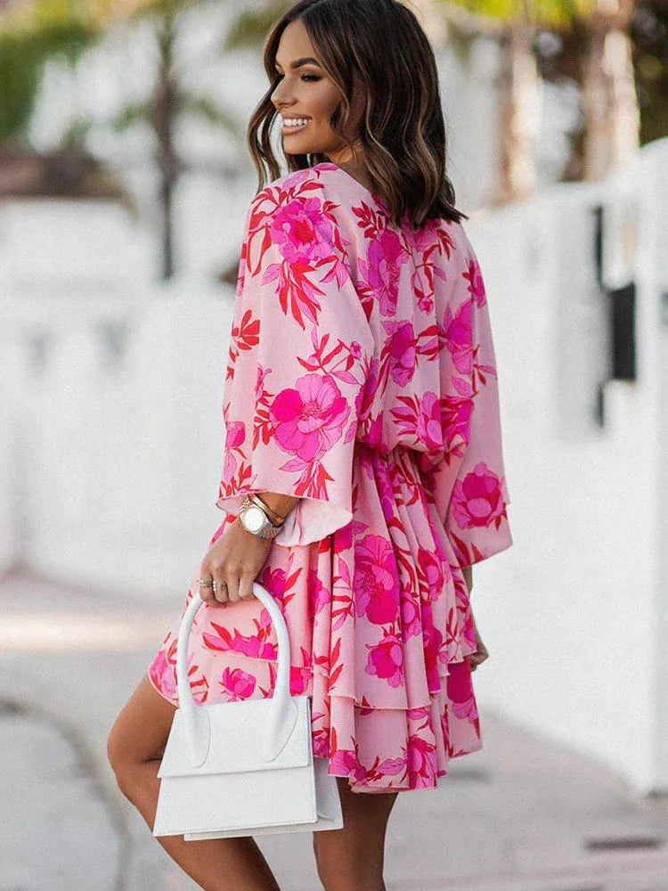 Feminines, kurzes Kleid mit floralem Print in Rosa, V-Ausschnitt und langen Ärmeln. Perfekt für Sommermode und elegante Anlässe.