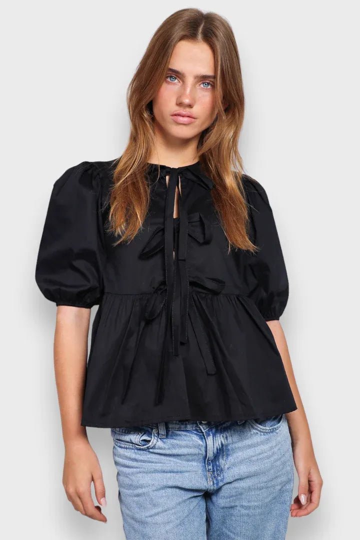 Schwarze Bluse mit Puffärmeln und Schleifen-Details, kombiniert mit blauen Jeans. Modetrend, Damenmode, stilvolles Outfit, lässiger Look.