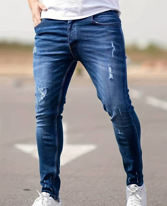 Mann in blauer, zerrissener Jeans und weißen Sneakern auf Straße stehend.