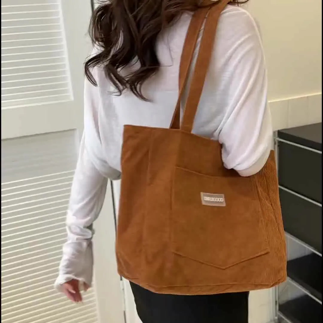 Braune Cord-Tasche mit Außentasche, getragen von einer Person in weißem Oberteil. Modische, geräumige Umhängetasche für Alltag und Shopping.