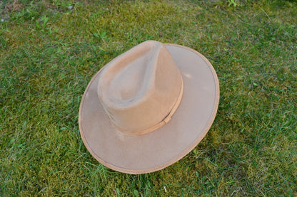 Breiter, beiger Filzhut auf grünem Gras. Perfekt für Outdoor-Abenteuer, stilvoll und funktional. Ideal für Wanderungen und Sonnenschutz.
