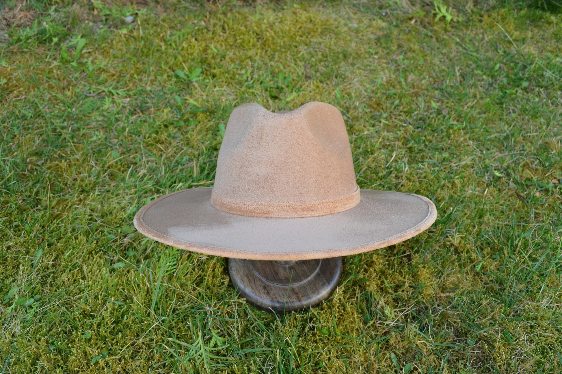Breiter Filzhut aus beigem Wildleder auf grünem Gras. Perfekt für Outdoor-Abenteuer, stilvoll und robust. Ideal für Herrenmode und Accessoires.