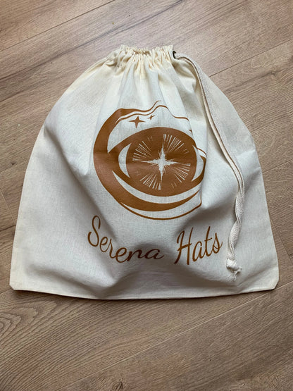 Baumwolltasche mit Kordelzug, bedruckt mit "Serena Hats" Logo, ideal für umweltfreundliche Aufbewahrung und Transport von Hüten.