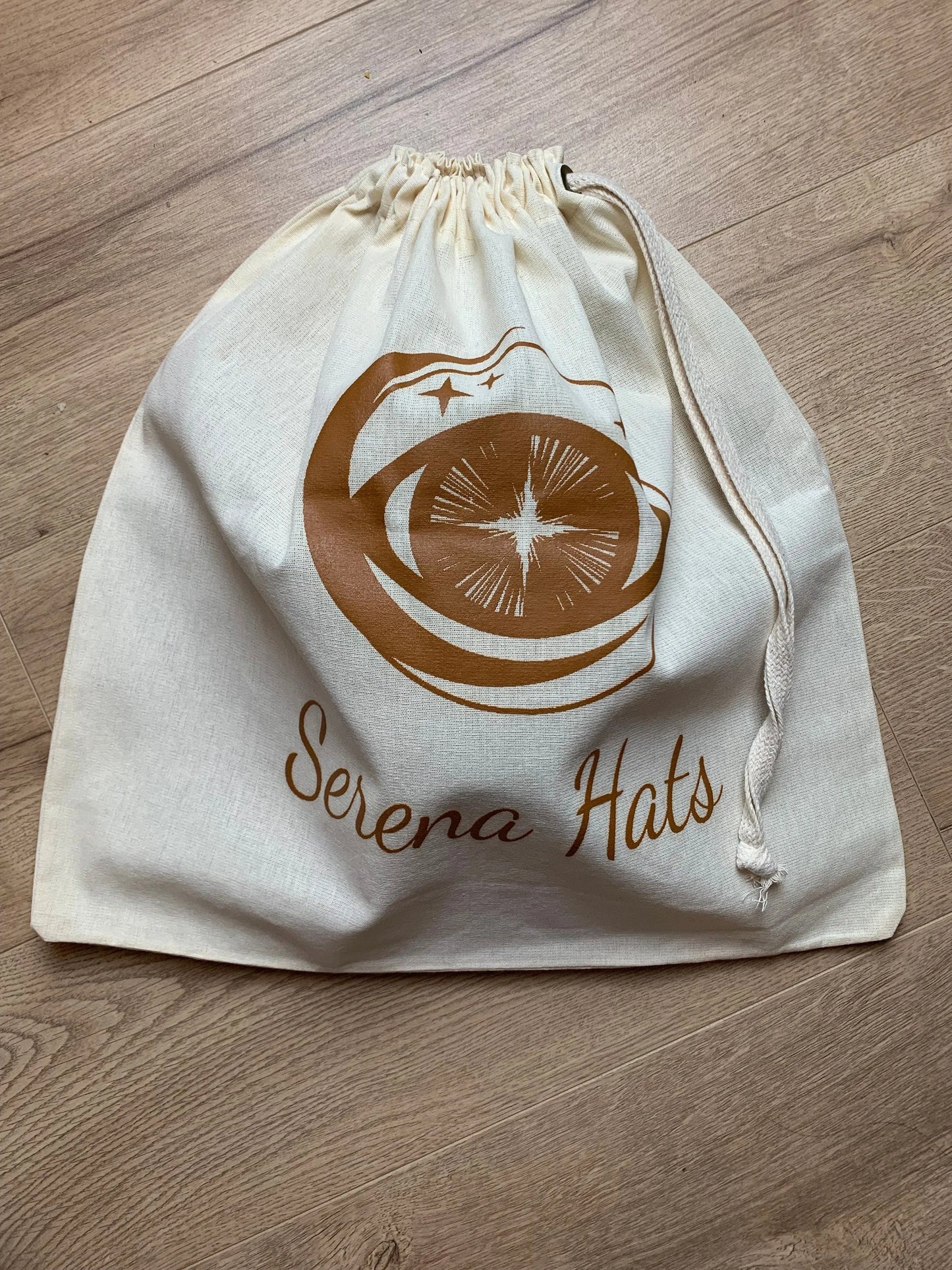 Baumwolltasche mit Kordelzug, bedruckt mit "Serena Hats"-Logo. Perfekt für umweltfreundliche Aufbewahrung und Transport von Hüten.