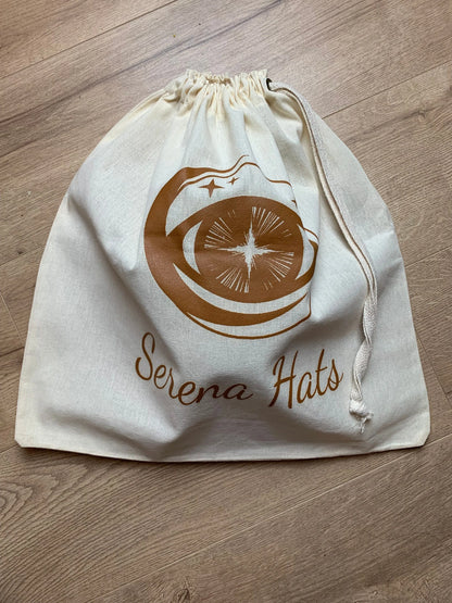 Baumwolltasche mit Kordelzug, bedruckt mit "Serena Hats"-Logo. Perfekt für umweltfreundliche Aufbewahrung und Transport von Hüten.